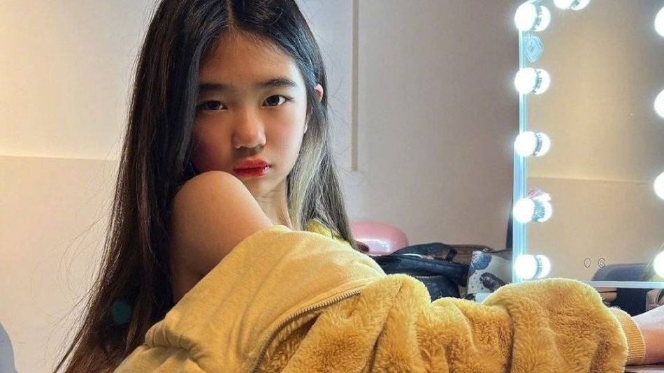 曹格女儿Grace留着一头长发，衣服滑落露出肩膀，对着镜头放电的模样