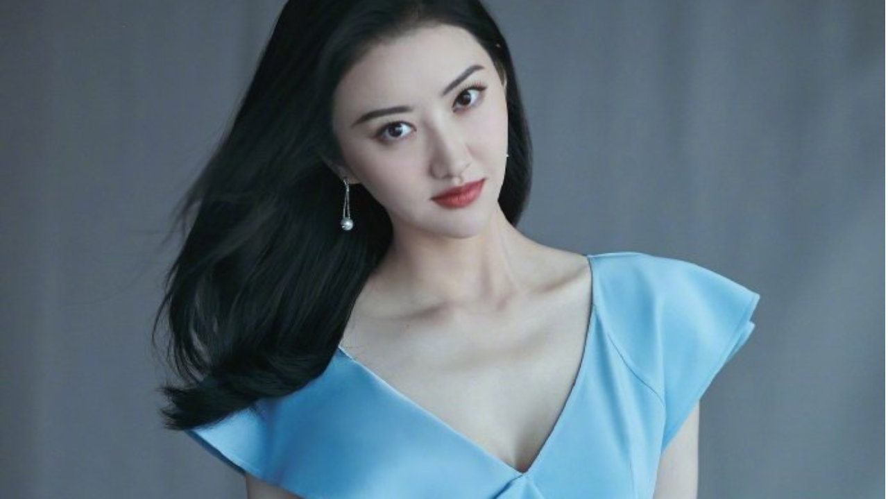 景甜身穿浅蓝色深V不规则长裙，手拿海螺，长发飘飘