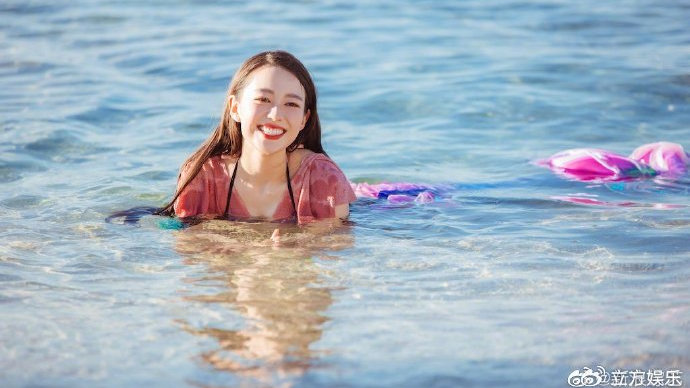 吉娜身穿美人鱼泳装凸显好身材，海边侧卧玩耍笑容灿烂。