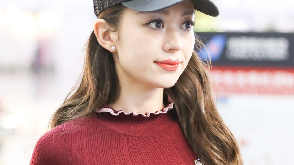 吉娜戴着黑色棒球帽身穿橘红色上衣和灰色裤子，大秀纤腰长腿身材完美