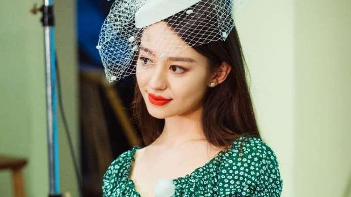 吉娜身着绿色碎花裙，笑容甜美，尽显清新俏皮。搭配白色发饰十分减龄