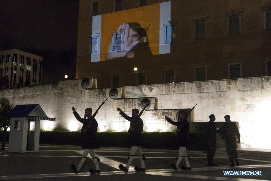 Members of the Presidential Guard walk past the Greek Parliament building on which a projection saying 