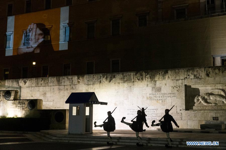 Members of the Presidential Guard walk past the Greek Parliament building on which a projection saying 