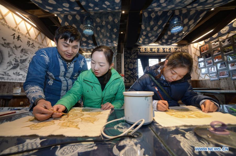 Wang Fangzhou (1st, L) guides a tourist in drawing batik patterns at a batik workshop in Danzhai County of Guizhou Province in southwest China, Dec. 1, 2020. Wang Fangzhou, 40, started in August 2016 a workshop specialized in batik, a craft inherited through generations among the Miao ethnic group in Guizhou. Later on, he launched a batik experience gallery in Wanda Township, a local tourist attraction. His workshop and gallery have received more than 6,000 tourists so far this year with combined sales revenue of over 300,000 yuan (about 45,500 U.S. dollars). Thirteen residents relocated from poverty-stricken areas have found employment with decent salaries here. (Xinhua/Yang Ying)