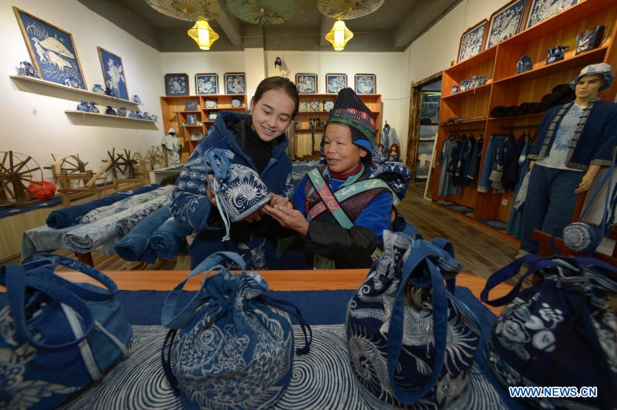 A sales assistant (L) and a resident relocated from poverty-stricken area observe a batik product at a batik workshop in Danzhai County of Guizhou Province in southwest China, Dec. 1, 2020. Wang Fangzhou, 40, started in August 2016 a workshop specialized in batik, a craft inherited through generations among the Miao ethnic group in Guizhou. Later on, he launched a batik experience gallery in Wanda Township, a local tourist attraction. His workshop and gallery have received more than 6,000 tourists so far this year with combined sales revenue of over 300,000 yuan (about 45,500 U.S. dollars). Thirteen residents relocated from poverty-stricken areas have found employment with decent salaries here. (Xinhua/Yang Ying)