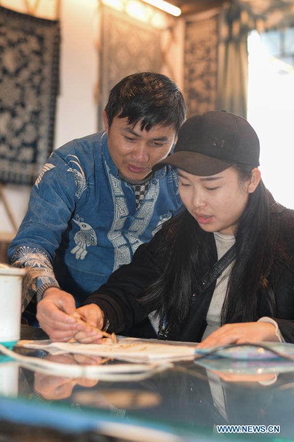 Wang Fangzhou (L) guides a tourist in drawing batik patterns at a batik experience gallery in Danzhai County of Guizhou Province in southwest China, Dec. 1, 2020. Wang Fangzhou, 40, started in August 2016 a workshop specialized in batik, a craft inherited through generations among the Miao ethnic group in Guizhou. Later on, he launched a batik experience gallery in Wanda Township, a local tourist attraction. His workshop and gallery have received more than 6,000 tourists so far this year with combined sales revenue of over 300,000 yuan (about 45,500 U.S. dollars). Thirteen residents relocated from poverty-stricken areas have found employment with decent salaries here. (Xinhua/Yang Ying)