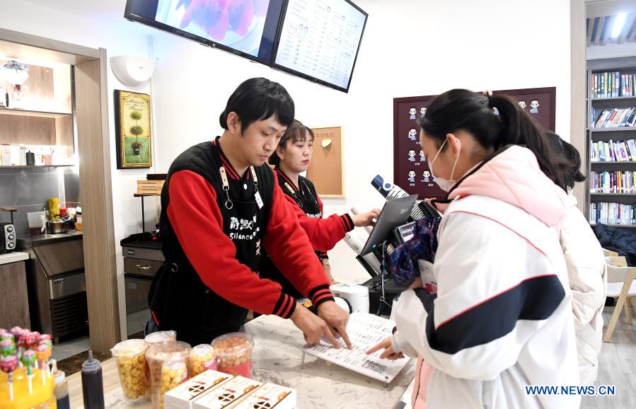 Staff members Li Tao and Cao Ruihua take orders for customers in Silence Coffee in Xincheng District of Xi'an, northwest China's Shaanxi Province, Dec. 1, 2020. Silence Coffee, a coffee shop opened in Xi'an more than two months ago, is also a business incubator established for disabled people. Three of the four staff members in Silence Coffee are hearing-impaired baristas. They communicate with customers with sign language or typing on cellphone. Working on two shifts, all four members carried out routine work in the coffee shop including coffee making, baking, guest receiving and cleaning. Wang Lichao, manager of Silence Coffee, has learned sign language so as to better guide and 