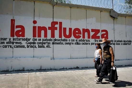 2009年,墨西哥城,戴着防护性外科口罩的民众走过甲型H1N1流感警告标志。