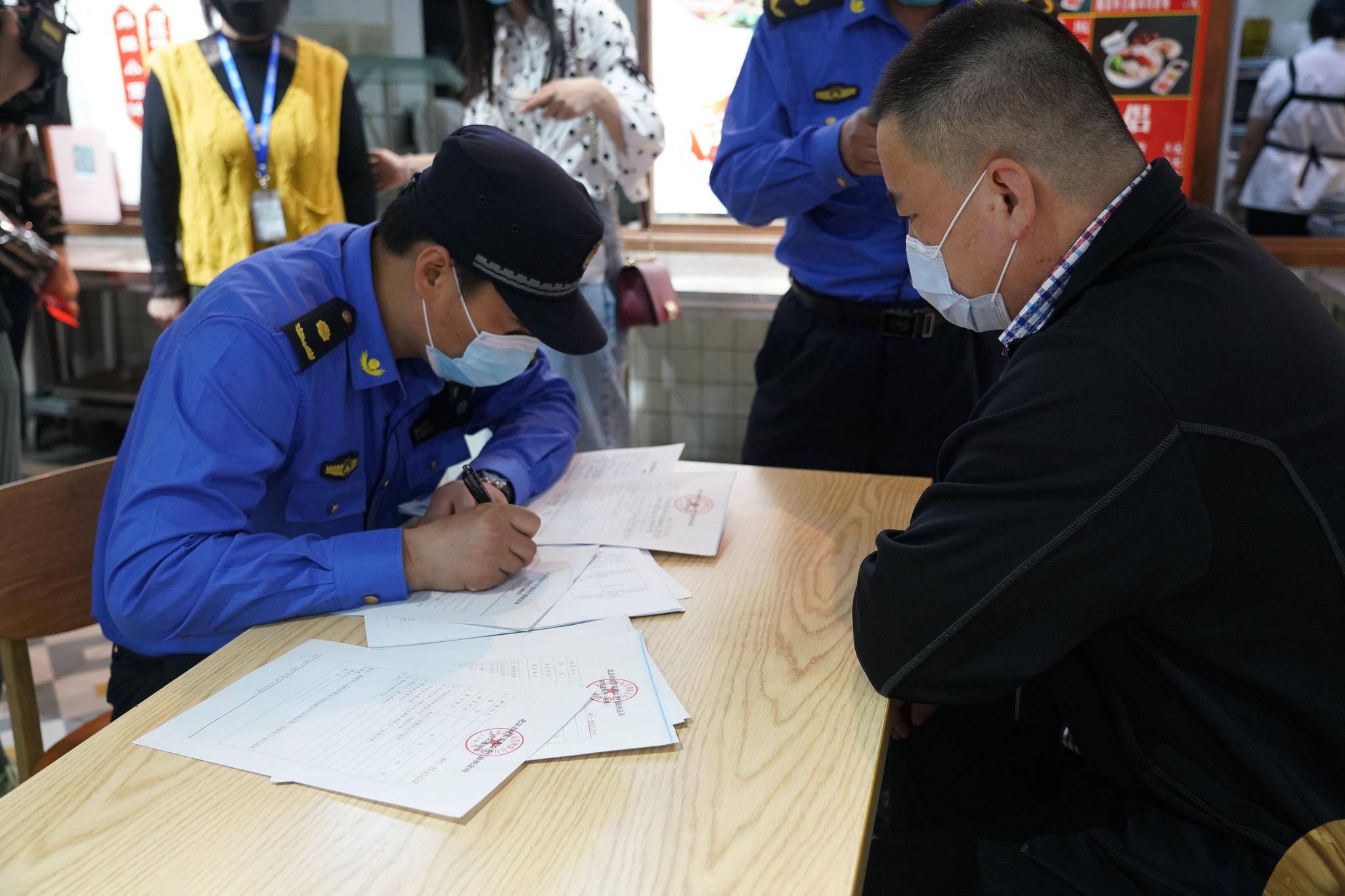 物美超市大成店，执法人员就现场发现的问题向超市负责人开具责令改正通知书。新京报记者 侯少卿 摄