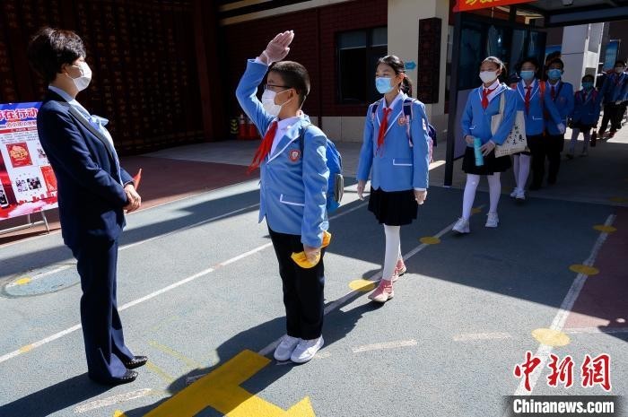 学生们佩戴口罩、间隔排队,次第通过自动测温门,进入校园。 韦亮 摄