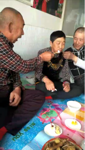  养母生日时，马吉明（右一）和养父给养母喂蛋糕。受访者供图
