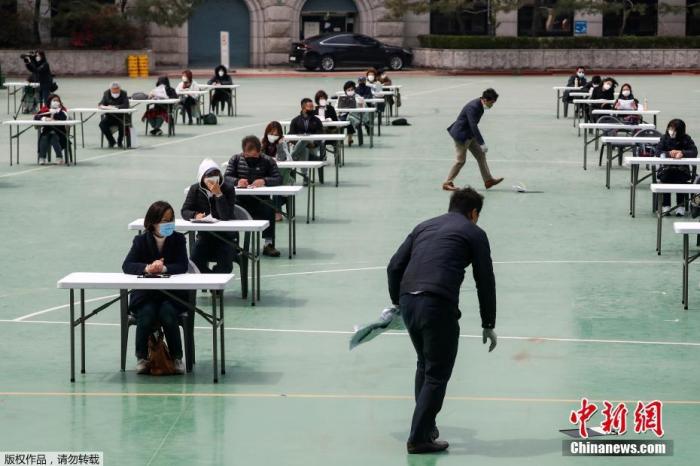 资料图:韩国为了避免新型冠状病毒传播,在露天操场为求职者举行入职考试。图为监考人员在地上捡起被风吹掉的文件。