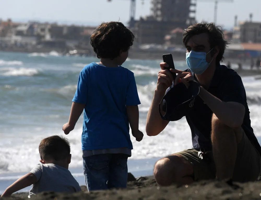 意大利首都罗马附近的拉迪斯波利，一名戴着口罩的男子给他的孩子拍照。新华社图