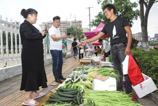 ▲6月1日,长沙市先锋街道老甫冲路,路边卖蔬菜的摊贩老板开心地让顾客扫码。图/记者张云峰