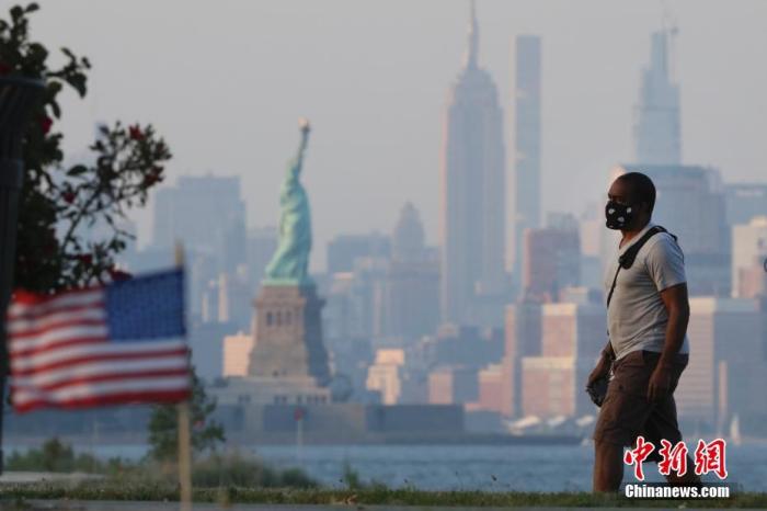 当地时间7月4日，一位居民戴着口罩从纽约曼哈顿对岸的海滨走过。中新社记者 廖攀 摄