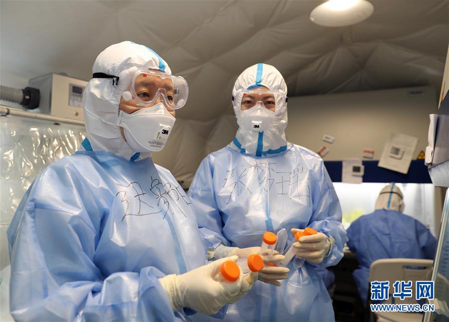 迟象阳博士(左)与张梦瑶博士(中)在负压帐篷实行室内开展抗体检测(3月23日摄)。新华社发(张振威 摄)