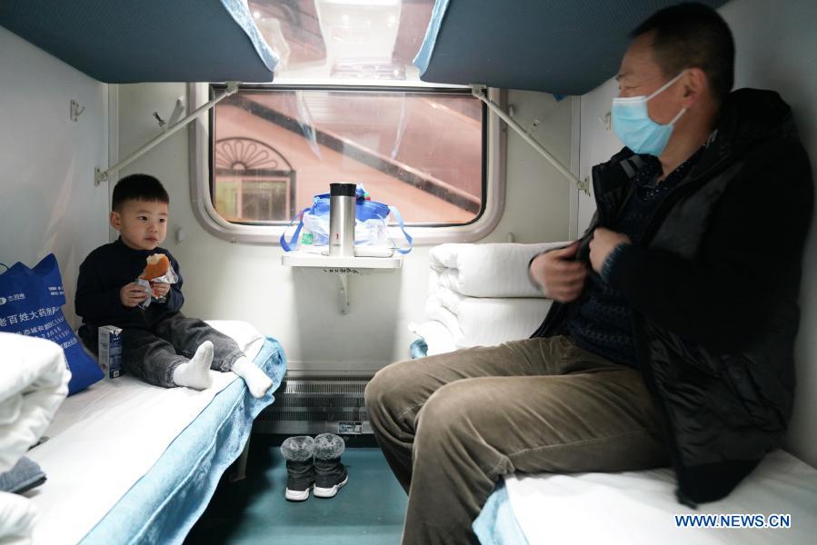 A passenger is seen with a child on train K7093 running from Harbin, northeast China's Heilongjiang Province to Hailar, north China's Inner Mongolia Autonomous Region, Jan. 6, 2021. Train No. K7093/4, connecting Harbin and Hailar, runs a distance of 1,320 kilometers and stops at 52 stations during the about 26-hour trip. The train stops every 30 minutes on average due to so many stops and is known as the slowest train in the forest area between the two destinations. Having operated for over 30 years, the train's facilities have witnessed upgrade and created a cozy environment for passengers. (Xinhua/Wang Jianwei)