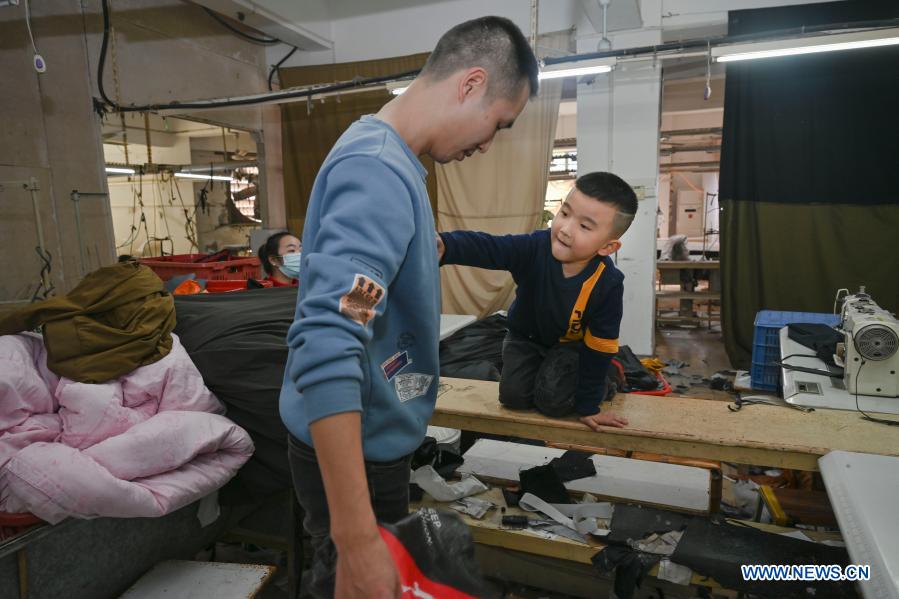 Congcong helps remove cotton on the clothes of his father Huang Hailong at a garment factory in Shishi, southeast China's Fujian Province, Jan. 26, 2021. Following the resurgence of sporadic COVID-19 cases, many places across China have encouraged residents and migrant workers to stay put to celebrate the Spring Festival, to reduce the flow of personnel and curb the spread of the coronavirus during the holiday period. Huang Hailong, a migrant worker in Shishi, said it would be his first time in past years to spend the holiday in Shishi instead of his hometown in the city of Suining, southwest China's Sichuan Province. Although living with his wife and younger son Congcong, Huang is still missing his parents and elder son who live in the hometown. He made down jackets, protective sleeves, pillows and aprons for them and posted those gifts back home. (Xinhua/Song Weiwei)