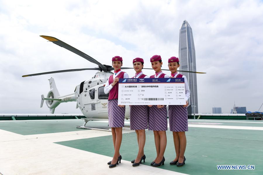 Flight attendants hold a large-size air ticket at the maiden flight ceremony of a newly introduced airport helicopter shuttle service on a helipad in downtown Shenzhen, south China's Guangdong Province, March 18, 2021. The Shenzhen civil aviation authority on Thursday launched a helicopter shuttle service between Shenzhen Bao'an International Airport and Futian District, the city's central business district. The flight route passes many urban landmarks of Shenzhen, and travel time can be as short as 10 minutes. At present, the service is provided only to passengers arriving from Beijing Daxing International Airport. (Xinhua/Mao Siqian)