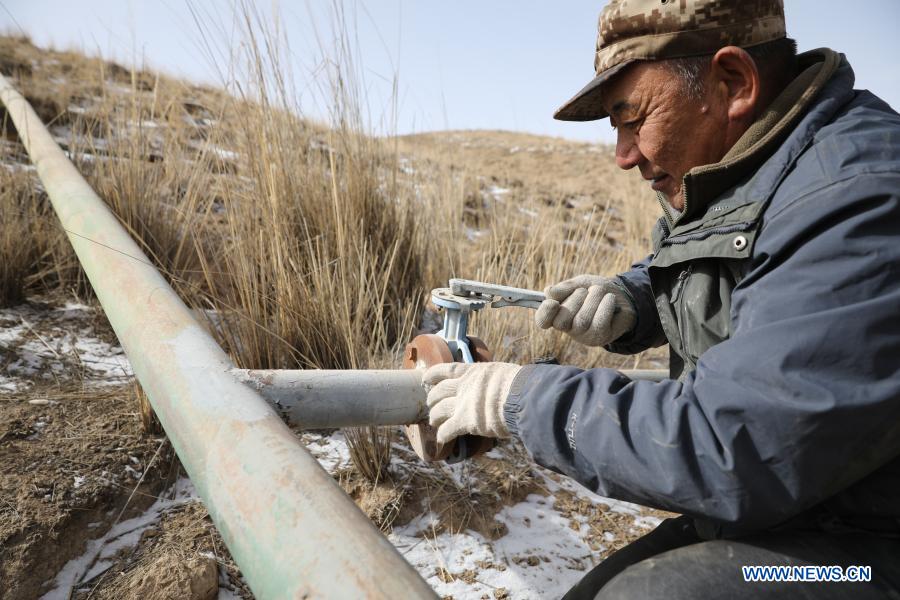 Gu Zhengli inspects the pipeline in Dahe Township, Yugu Autonomous County of Sunan, northwest China's Gansu Province, March 20, 2021. Gu Zhengli, 59, has been working at the frontline of Tanggaer water conservancy project in Dahe Township for 42 years, safeguarding the safety of the drinking water for local people and livestock. As the annual rainfall in the town is only 150 to 300 millimeters, Tanggaer water conservancy project is literally the lifeline for local herdsmen. Every morning, Gu gets up early and operates a pump to move water from the pumping station at the foot of the mountain to a reservoir at the top. Then he climbs to the top of the mountain at about 7 o'clock and opens the valve, letting the water in the reservoir flow to each water supply point through 7 pipelines. After that, he rides a motorcycle to 52 water supply points to check if everything runs well. In the past 42 years, Gu has been working like this. Local herdsmen always see him busy on the way along the water conservancy project. Thanks to the efforts of Gu and his colleagues, people in the area now can not only enjoy much safer water but also achieve a balance between grass and livestock ahead of schedule. At a drinking well along the water conservancy project, local herdsmen wrote a sign which says 