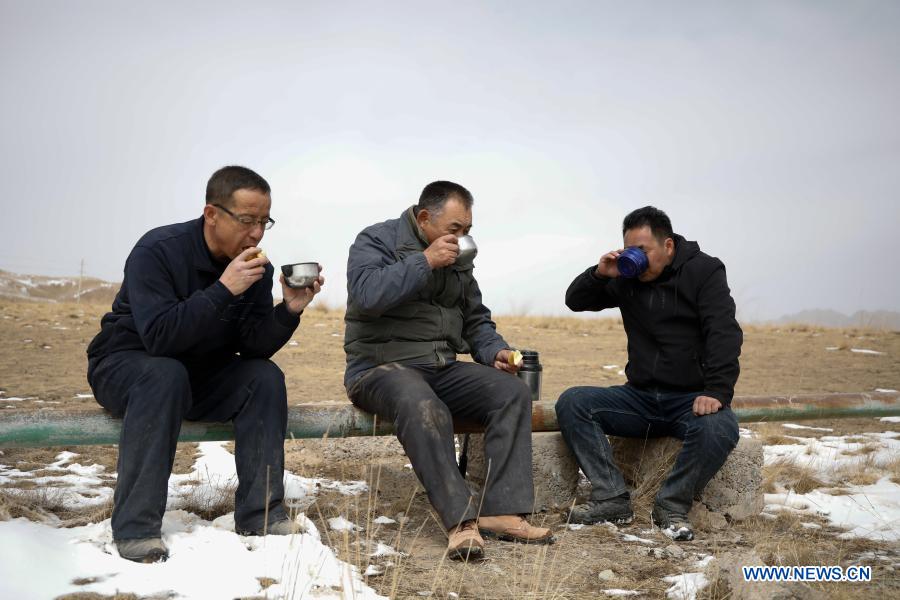 Gu Zhengli (C) has lunch with his colleagues during an inspection tour in Dahe Township, Yugu Autonomous County of Sunan, northwest China's Gansu Province, March 20, 2021. Gu Zhengli, 59, has been working at the frontline of Tanggaer water conservancy project in Dahe Township for 42 years, safeguarding the safety of the drinking water for local people and livestock. As the annual rainfall in the town is only 150 to 300 millimeters, Tanggaer water conservancy project is literally the lifeline for local herdsmen. Every morning, Gu gets up early and operates a pump to move water from the pumping station at the foot of the mountain to a reservoir at the top. Then he climbs to the top of the mountain at about 7 o'clock and opens the valve, letting the water in the reservoir flow to each water supply point through 7 pipelines. After that, he rides a motorcycle to 52 water supply points to check if everything runs well. In the past 42 years, Gu has been working like this. Local herdsmen always see him busy on the way along the water conservancy project. Thanks to the efforts of Gu and his colleagues, people in the area now can not only enjoy much safer water but also achieve a balance between grass and livestock ahead of schedule. At a drinking well along the water conservancy project, local herdsmen wrote a sign which says 