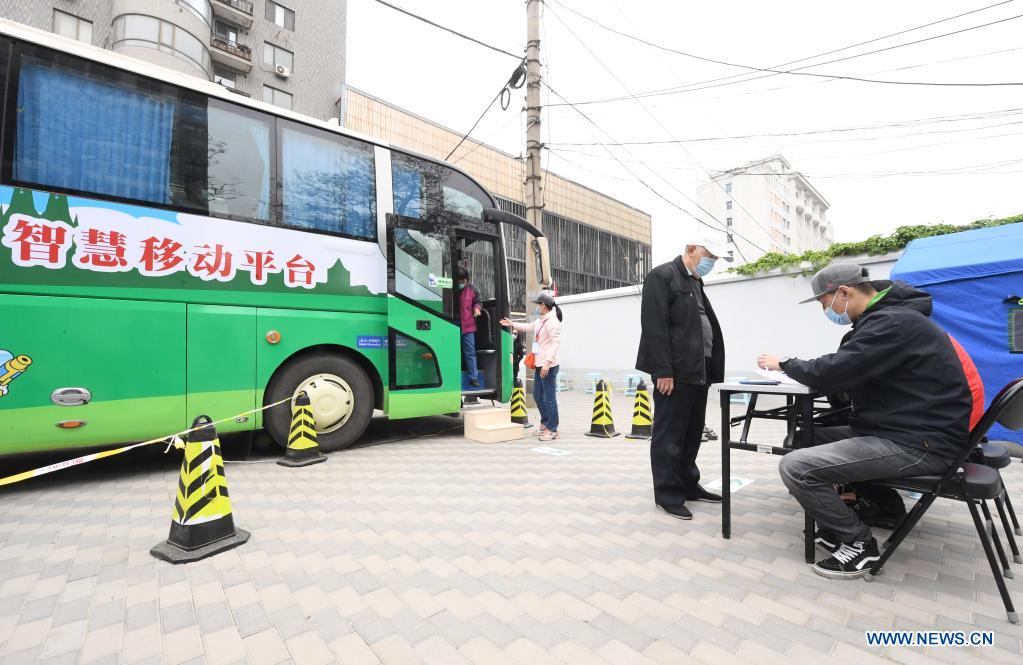 Community workers fill in an observation card for a man after he receiving a COVID-19 vaccine outside a mobile vaccination vehicle in Haidian District of Beijing, capital of China, April 11, 2021. Beijing and Shanghai have deployed mobile vaccination vehicles in downtown areas. The bus-like facilities, equipped with vaccination stations, medical refrigerators and first-aid equipment, have been rolled out to save time and improve inoculation efficiency. (Xinhua/Ren Chao)