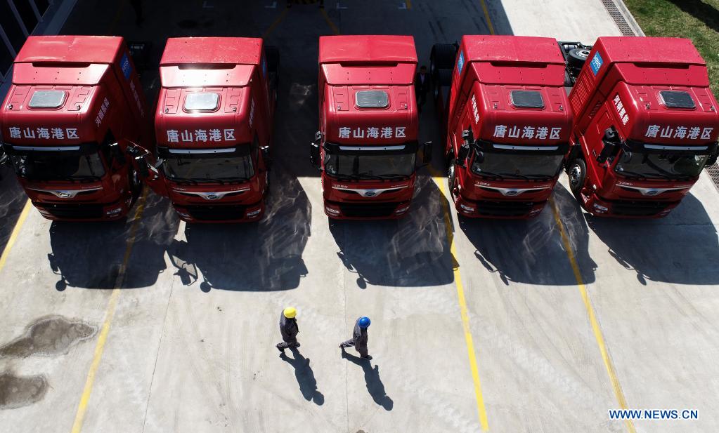 Photo taken with a drone shows workers walking past five newly introduced hydrogen-powered heavy-duty trucks in the Tangshan Haigang Economic Development Zone of Tangshan, north China's Hebei Province, April 14, 2021. Five hydrogen-powered heavy-duty trucks have been introduced on Wednesday by the Tangshan Haigang Economic Development Zone. The fleet of trucks are among the zone's first attempts to optimize its industrial structure and energy consumption by gradually replacing diesel fuel with the more eco-friendly hydrogen power cells. (Xinhua/Yang Shiyao)