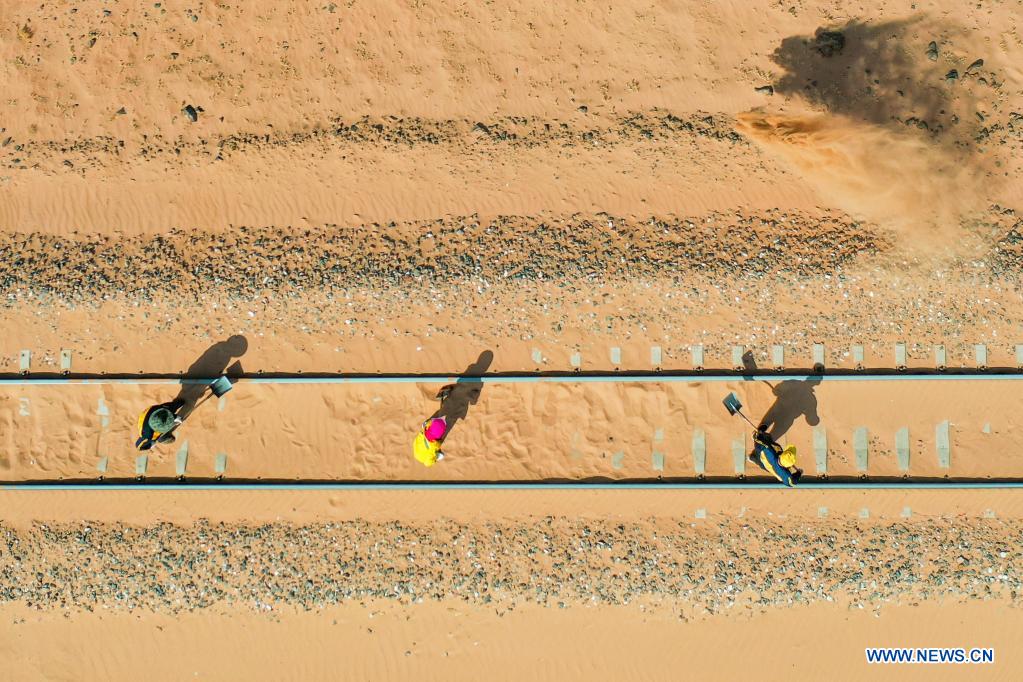 Aerial photo shows workers removing sand along Linhe-Ceke railway in north China's Inner Mongolia Autonomous Region, April 14, 2021. With a total length of 768 kilometers, the Linhe-Ceke railway is one of the important junctions connecting Mongolia and China. Two passenger trains and nearly 40 freight trains run on it every day. In order to control the sand damage, eleven sand control stations have been set up along the Linhe-Ceke railway that traverses more than 400 kilometers of desert. The railway sand control workers are stationed here all year round to prevent the accumulation of quicksand on the railway lines and ensure the smooth railway transportation. (Xinhua/Lian Zhen)