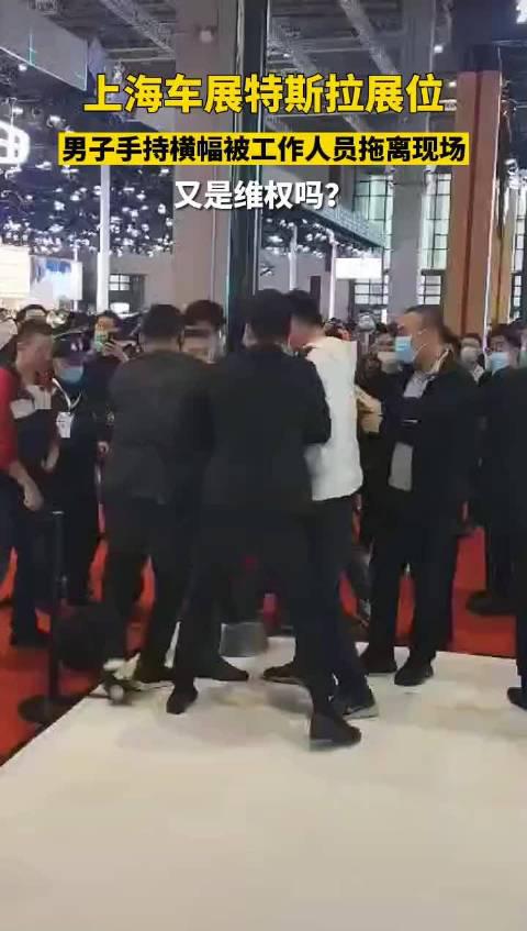 上海车展特斯拉展位，男子手持横幅被工作人员拖离现场……