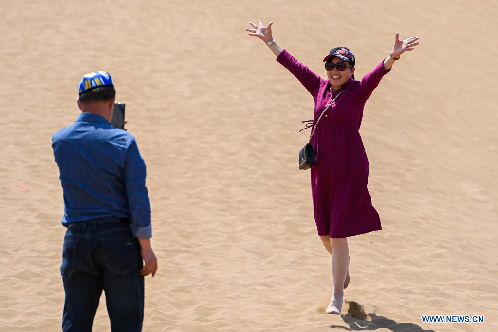 A tourist poses for photos in Kumtag Desert in Shanshan County, northwest China's Xinjiang Uygur Autonomous Region, May 15, 2021. The county sees boom in desert tourism early May. (Xinhua/Ding Lei)