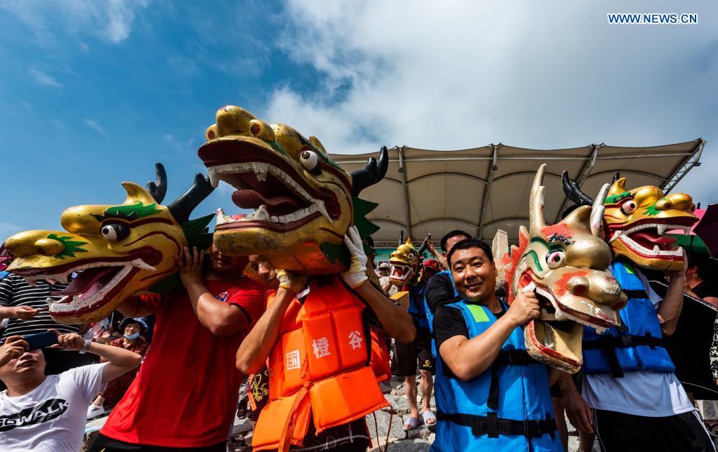 Participants carry the dragon boat heads to the river before a dragon boat race to celebrate the Dragon Boat Festival in Zigui County, central China's Hubei Province, June 14, 2021. China celebrated the Dragon Boat Festival on Monday to commemorate Qu Yuan, a patriotic poet from the Warring States Period (475-221 BC) believed to have been born in Zigui County. (Photo by Zheng Jiayu/Xinhua)