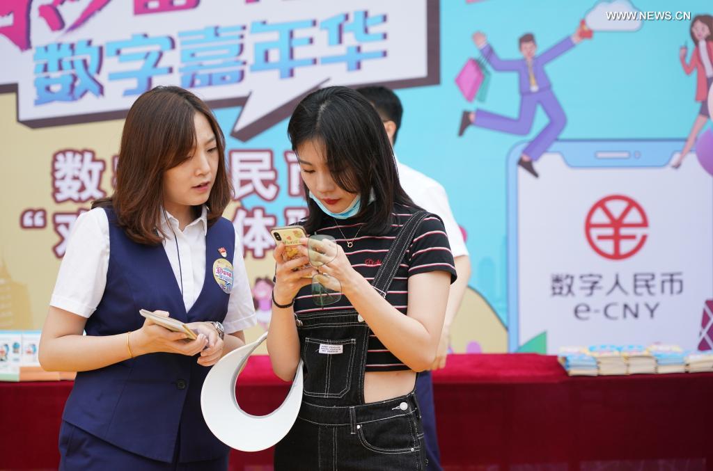 A staff member (L) of the Bank of Communications helps as a tourist tries the online wallet of digital RMB at the Happy Valley Beijing theme park the in Beijing, capital of China, June 16, 2021. (Xinhua/Chen Zhonghao)