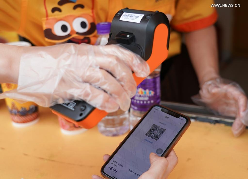 A staff member receives money from a tourist using digital RMB with a POS reader at the Happy Valley Beijing theme park the in Beijing, capital of China, June 16, 2021. (Xinhua/Chen Zhonghao)