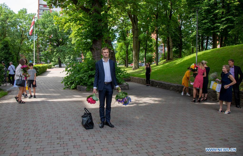 People hold bunches of flowers to wait for students attending a graduation ceremony outside Riga Stradins University in Riga, Latvia, on June 29, 2021. (Photo by Edijs Palens/Xinhua)