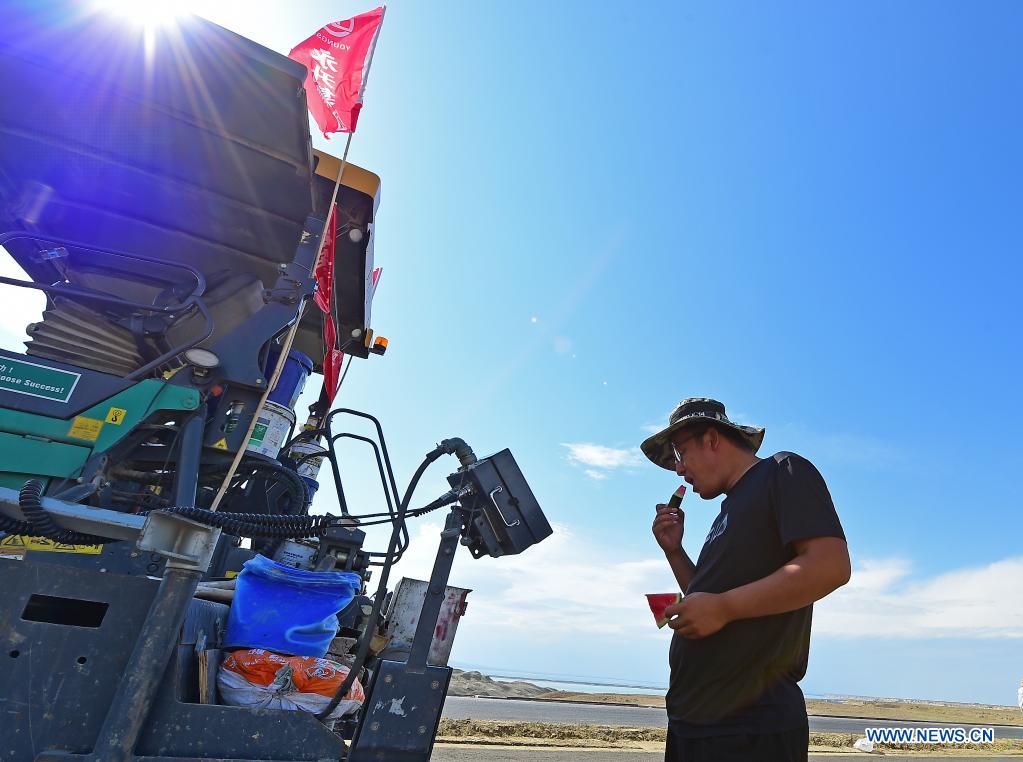 A worker eats watermelon to cool himself off at a construction site of a cross-desert expressway in northwest China's Xinjiang Uygur Autonomous Region, July 16, 2021. Construction of the first cross-desert expressway in Xinjiang has proceeded smoothly. The expressway, linking Altay Prefecture and the regional capital city of Urumqi, stretches some 343 km, with sections of more than 150 km built through the desert. (Xinhua/Hou Zhaokang)