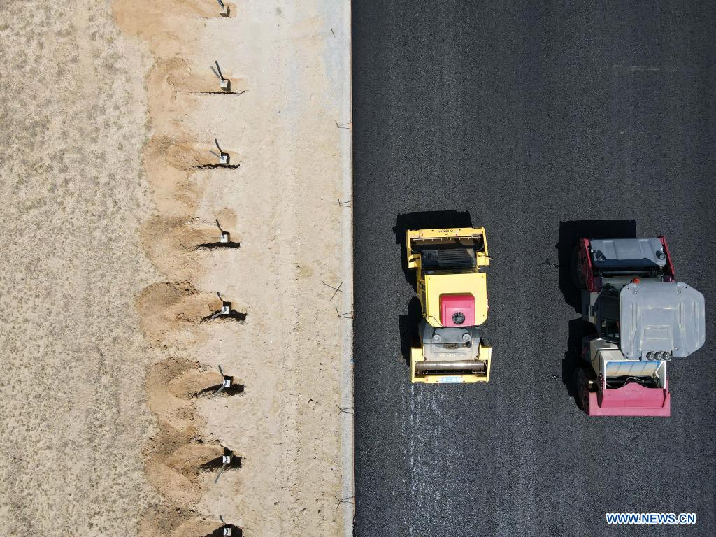 In this aerial photo, vehicles pave a section of a cross-desert expressway with asphalt in northwest China's Xinjiang Uygur Autonomous Region, July 16, 2021. Construction of the first cross-desert expressway in Xinjiang has proceeded smoothly. The expressway, linking Altay Prefecture and the regional capital city of Urumqi, stretches some 343 km, with sections of more than 150 km built through the desert. (Xinhua/Gao Han)