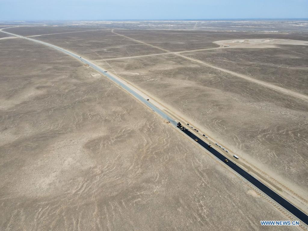 In this aerial photo, vehicles pave a section of a cross-desert expressway with asphalt in northwest China's Xinjiang Uygur Autonomous Region, July 16, 2021. Construction of the first cross-desert expressway in Xinjiang has proceeded smoothly. The expressway, linking Altay Prefecture and the regional capital city of Urumqi, stretches some 343 km, with sections of more than 150 km built through the desert. (Xinhua/Gao Han)