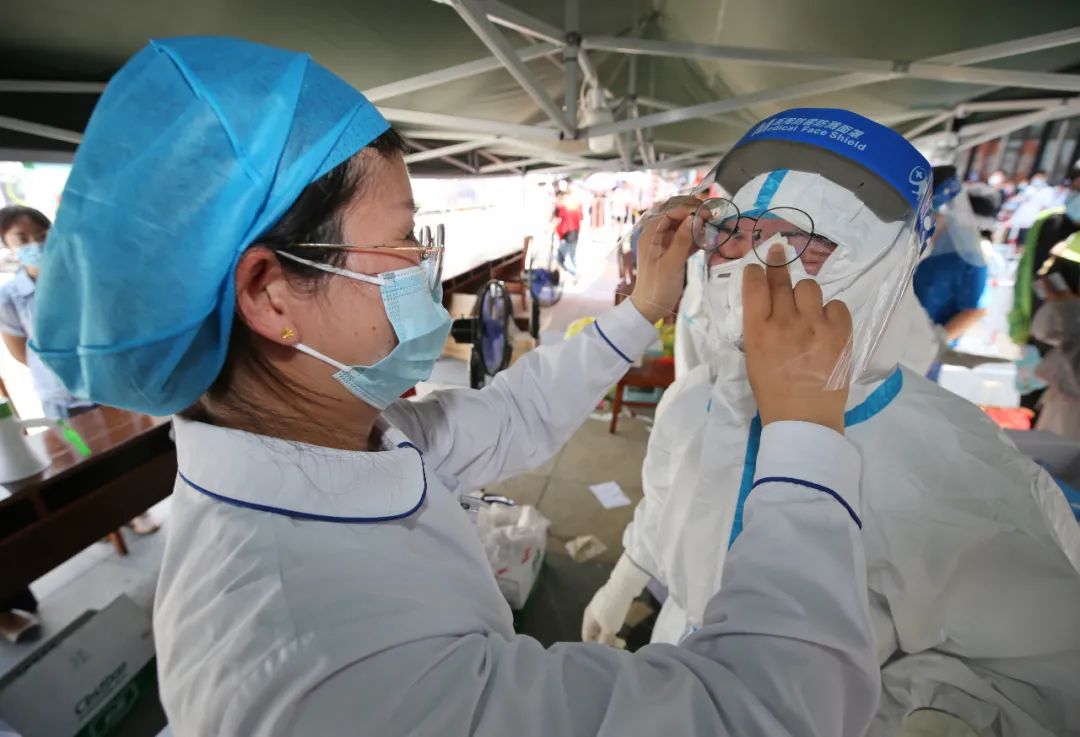 江宁区核酸检测点,工作人员在帮助身着防护服的医护人员擦汗。