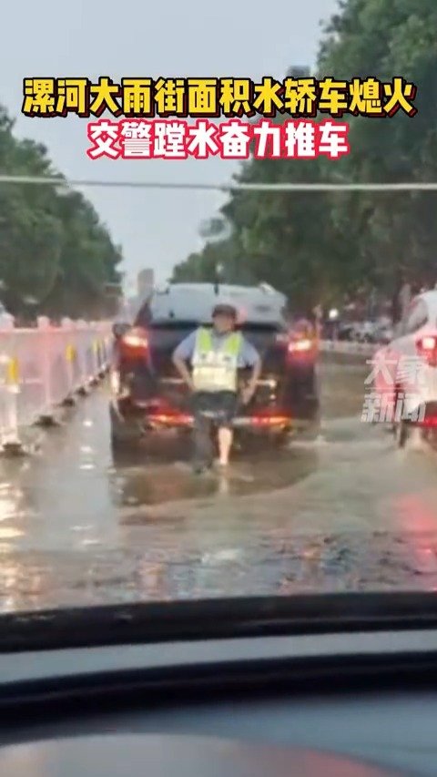 7月21日，河南漯河，街面积水轿车熄火，交警蹚水奋力推车