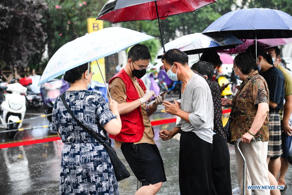 A volunteer (2nd L) works as local residents hold umbrellas for him at a stadium in Gulou District of Nanjing, capital of east China's Jiangsu Province, July 25, 2021. Nanjing, a mega-city with a population of more than 9.3 million, has launched a second round of all-inclusive nucleic acid testing and urged residents not to leave the city unless necessary. (Xinhua/Ji Chunpeng)