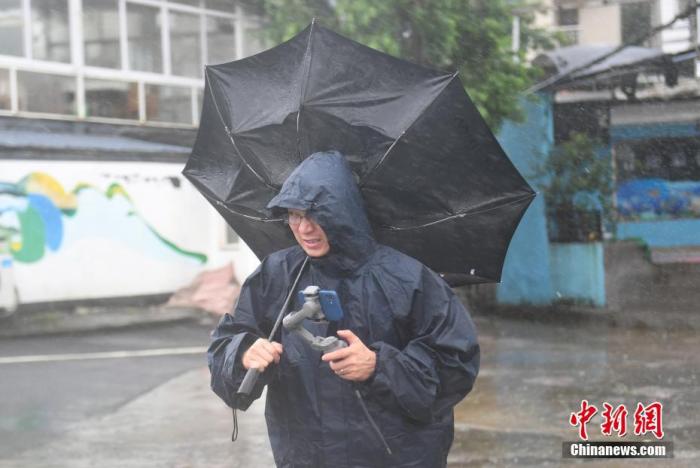 7月26日,浙江嘉兴,一名媒体记者的雨伞被吹翻。 中新社记者 王刚 摄