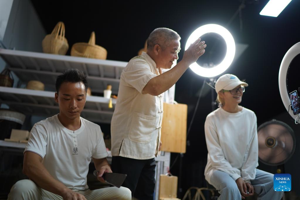 Li Nian'gen (C) and his team introduce bamboo products via livestreaming in Dongcun Township, Fenyi County, Xinyu City of east China's Jiangxi Province, Sept. 1, 2021. Li Nian'gen, 62, is the fifth-generation inheritor of bamboo-weaving techniques in Dongcun Township. Li acquired bamboo-weaving techniques from his uncle when he was barely nine years old, and started to make a living on his own at the age of 15. More than 20 of his apprentices chose to seek employment for better income in other walks of life away from home in early 1990s, but Li decided to stay and stick to his profession. Li occasionally demonstrated his bamboo-weaving techniques on a video clip platform as suggested by others in 2019, and became increasingly popular ever since then. Now Li has more than 8 million followers on different platforms, with his short videos popular among netizens. (Xinhua/Zhou Mi)