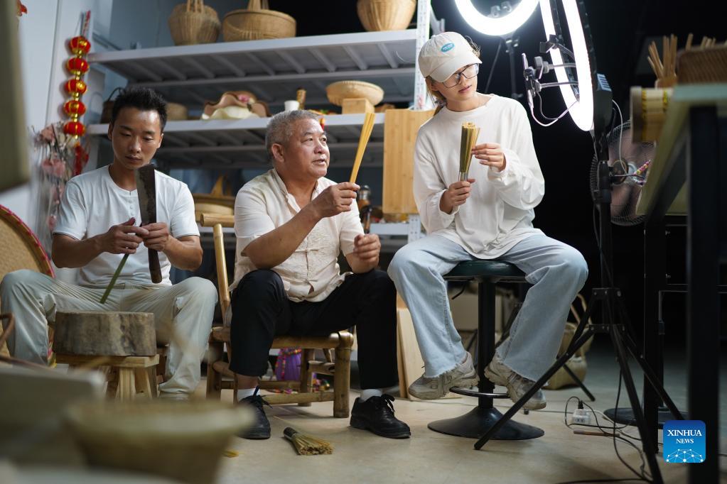 Li Nian'gen (C) and his team introduce bamboo products via livestreaming in Dongcun Township, Fenyi County, Xinyu City of east China's Jiangxi Province, Sept. 1, 2021. Li Nian'gen, 62, is the fifth-generation inheritor of bamboo-weaving techniques in Dongcun Township. Li acquired bamboo-weaving techniques from his uncle when he was barely nine years old, and started to make a living on his own at the age of 15. More than 20 of his apprentices chose to seek employment for better income in other walks of life away from home in early 1990s, but Li decided to stay and stick to his profession. Li occasionally demonstrated his bamboo-weaving techniques on a video clip platform as suggested by others in 2019, and became increasingly popular ever since then. Now Li has more than 8 million followers on different platforms, with his short videos popular among netizens. (Xinhua/Zhou Mi)