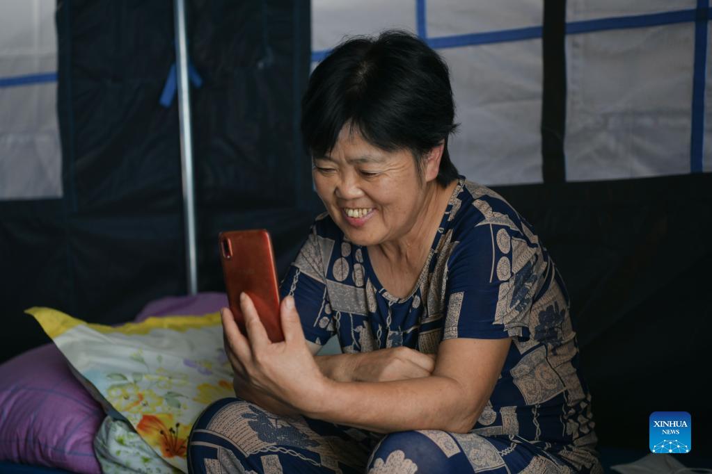 A woman chats with relatives via video call at a temporary resettlement site in Tuancang Village of Fuji Township of Luxian County, southwest China's Sichuan Province, Sept. 21, 2021. Residents from Sichuan Province who were affected by an earthquake that struck on Sept. 16 began returning home on Monday morning, as the local work priority has been shifted from emergency rescue to post-quake reconstruction. A 6.0-magnitude earthquake jolted Luxian County in the city of Luzhou at 4:33 a.m. on Sept. 16, leaving three people dead and 146 injured. (Xinhua/Xu Bingjie)