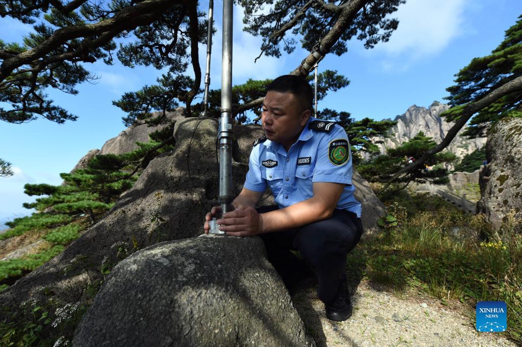 Hu Xiaochun checks the supporting poles of the Greeting Pine in the Huangshan Mountain scenic area in east China's Anhui Province, Sept. 26, 2021. Huangshan Mountain, one of the most famous scenic spots in China, is a UNESCO World Heritage site in east China's Anhui Province and a world geopark. Greeting Pine is a famous landmark in Huangshan Mountain. The tree, growing out of the rocks with a long branch extending over the mouth of a cave, got the name mainly because it appears to be greeting anyone who arrives at the scene. It is believed to be between 800 and 1,000 years old. To protect the tree, the local government has introduced a system of designating guardians or rangers for patrolling the tree around the clock. The first guardian was appointed in 1981. The tradition has been going on ever since. Hu Xiaochun is one of the guardians of the Greeting Pine. In 2010, Hu took over the post from his predecessor. He patrols around the Greeting Pine every two hours, observing subtle changes in branches, leaves and bark, as well as the supporting frames and cables. Hu records the tree growth data every day, and the temperature, humidity and wind speed. His 