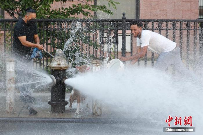 资料图：当地时间2020年7月27日，两名青年在纽约布鲁克林街道上喷水的消防栓前嬉水消暑。 中新社记者 廖攀 摄