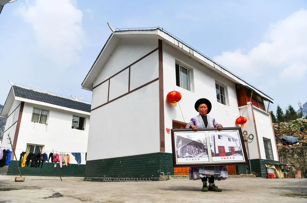 在贵州省黔西县新仁苗族乡化屋村麻窝寨易地扶贫搬迁集中安置点，搬迁户站在新房前展示自家搬迁前后的对比照片（2月20日摄）。新华社记者 杨文斌 摄