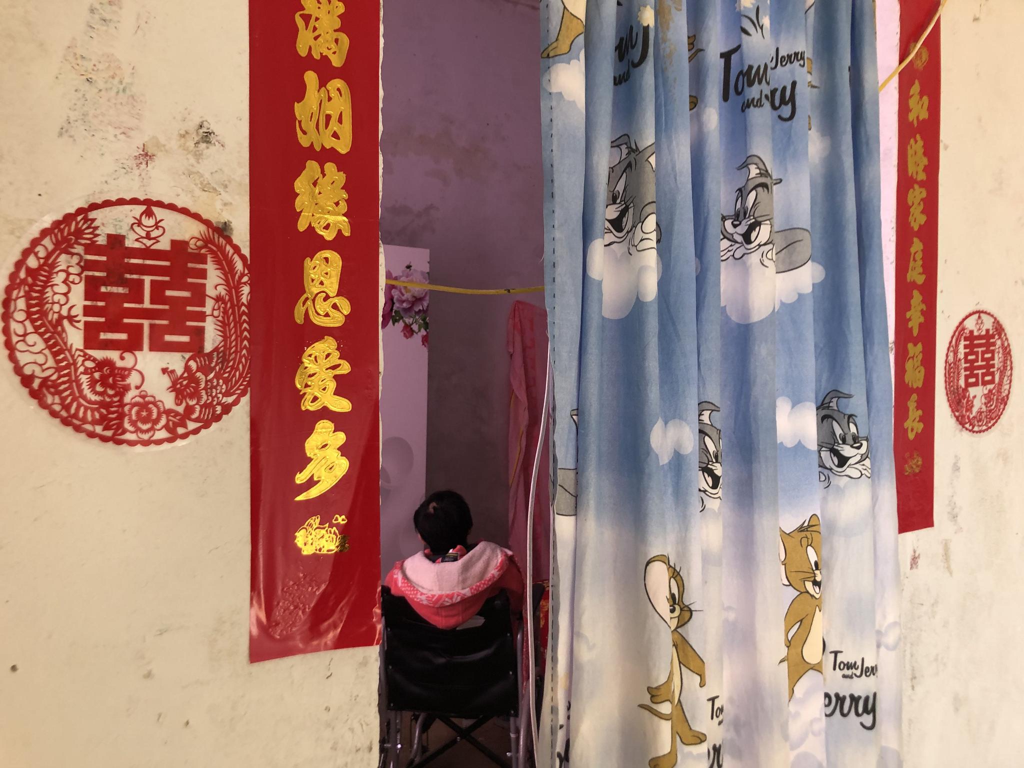 新娘坐在婚房的轮椅上,门口贴着新婚对联。新京报记者 杜寒三 摄
