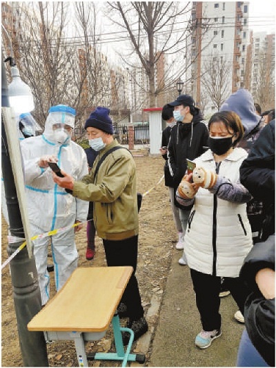  图为1月9日,天津市津南区检察院党员干警身穿防护服,在核酸检测现场维持疏导秩序,指导居民提前用手机做好检测预约登记。 