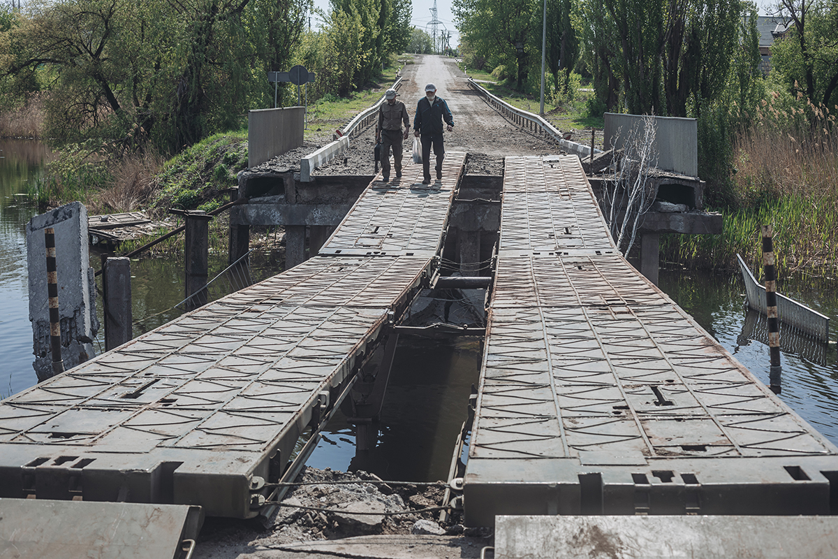 当地时间2022年5月8日，两名男子穿过乌克兰哈尔科夫郊区一座被毁坏的桥梁。